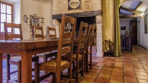 Un coin repas avec une table et des chaises en bois, un mur en pierre orné d’un tableau encadré et un sol carrelé.