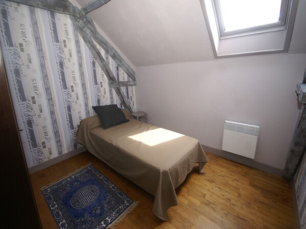 Una habitación pequeña con cama individual, techo inclinado, radiador y alfombra estampada.