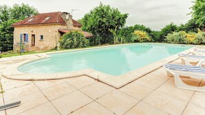 A swimming pool with a curved edge, surrounded by a tiled deck. - Holiday Home in Besse by Lake & Forest (Besse)