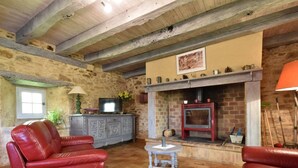 A rustic living room with a stone wall, a fireplace, leather sofas, and a television. - Holiday Home in Besse by Lake & Forest (Besse)