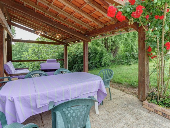 An outdoor patio with a covered seating area, a table with a purple tablecloth, and chairs.