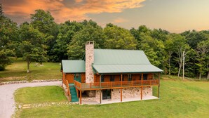 Un chalet doté d’une cheminée en pierre, d’une terrasse en bois et d’un toit végétalisé, entouré d’une végétation luxuriante.