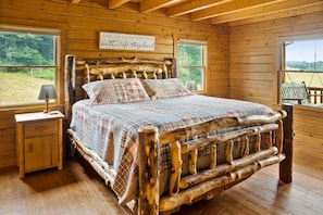 Un dormitorio de cabaña de madera con cama, mesita de noche y ventana con vistas al exterior.