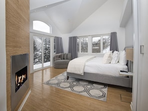 A modern bedroom with a fireplace, large windows, a gray sofa, and a patterned rug. - Apres Chalet (Vail)