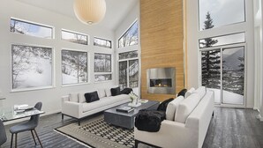 Un salon spacieux avec un canapé blanc, une cheminée, de grandes fenêtres et une vue sur un paysage enneigé.
