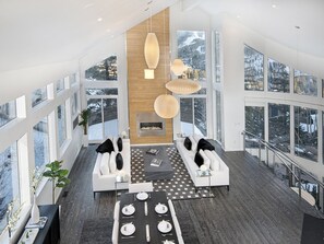 A modern living room with a fireplace, large windows, and a dining area. - Apres Chalet (Vail)