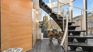 Un intérieur moderne avec un escalier à volutes, un mur en bois et de grandes fenêtres donnant sur une zone boisée.