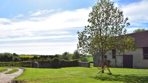 A rural landscape with a gravel path, a large tree, and a building with a red roof.
