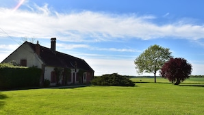 A large, single-story house with a sloped roof and a chimney, surrounded by a well-maintained lawn and a few trees.
