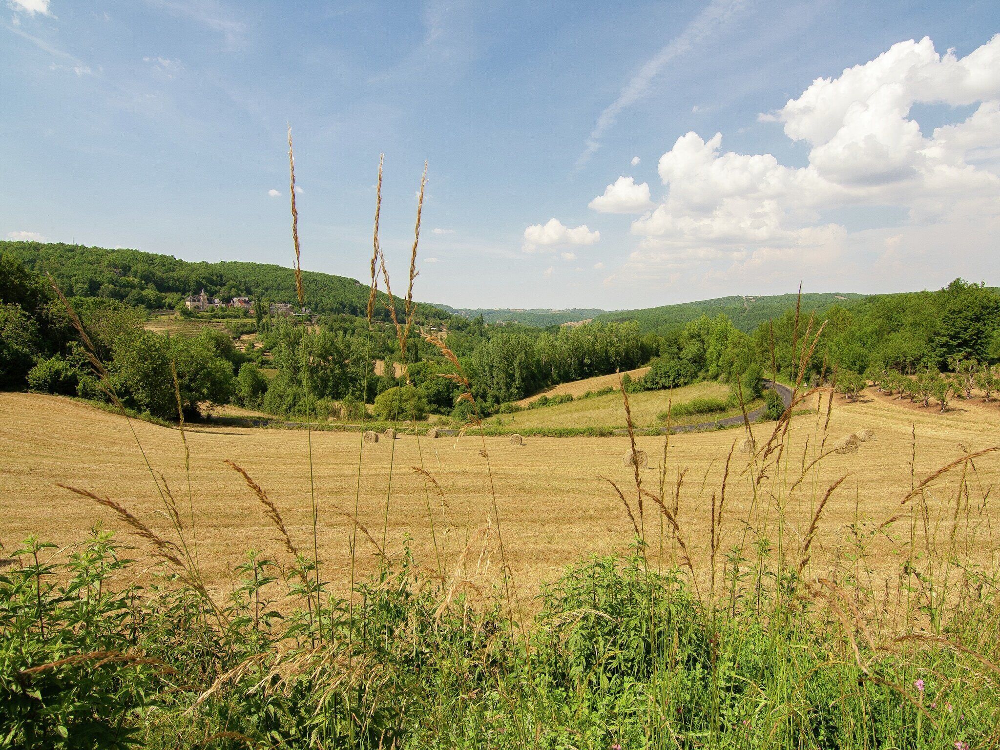 Een landelijk landschap met glooiende heuvels, een heldere lucht en een dorpje in de verte.