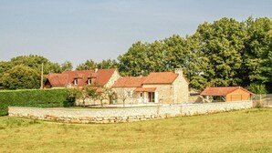 Een stenen huis met een rood dak, omgeven door een stenen muur en een grasveld.