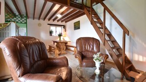 A spacious loft with high ceilings, exposed wooden beams, leather armchairs, a glass coffee table, and a wooden staircase.