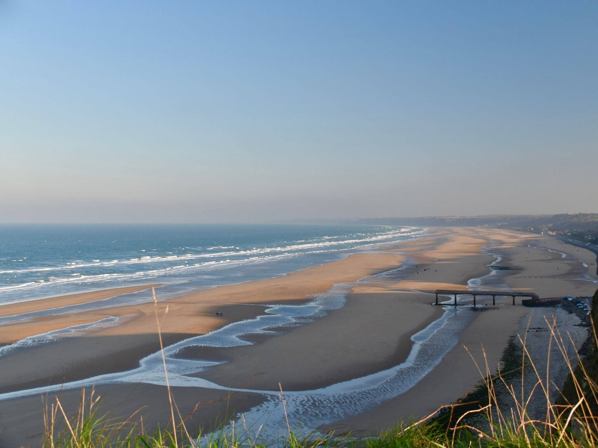 A coastal landscape with a wide sandy beach, gentle waves, and a clear sky.