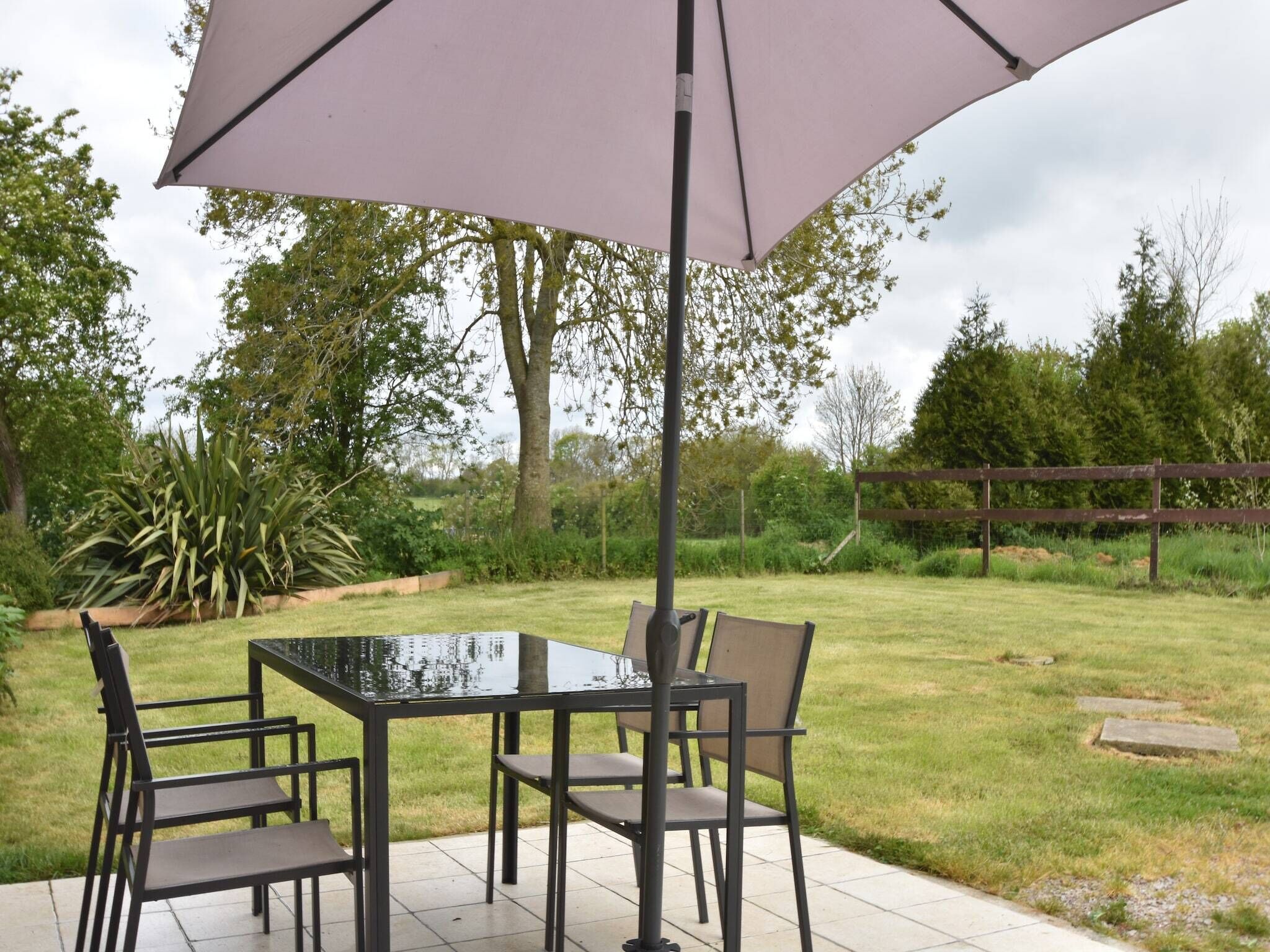 Een terras met een glazen tafel en stoelen, een parasol, en een houten hek op de achtergrond.