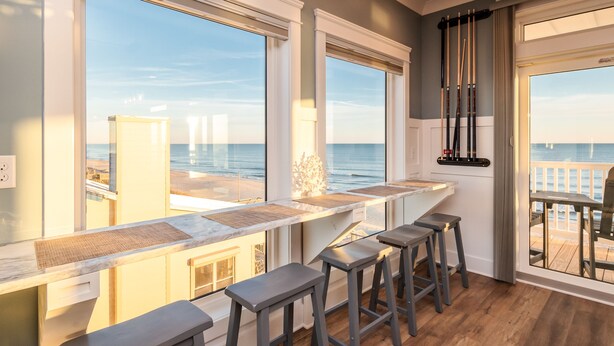 Una cocina con ventanas amplias, una barra con taburetes y vista al océano.