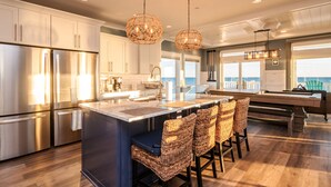 Una cocina moderna con electrodomésticos de acero inoxidable, una isla central con taburetes de bar e iluminación colgante.