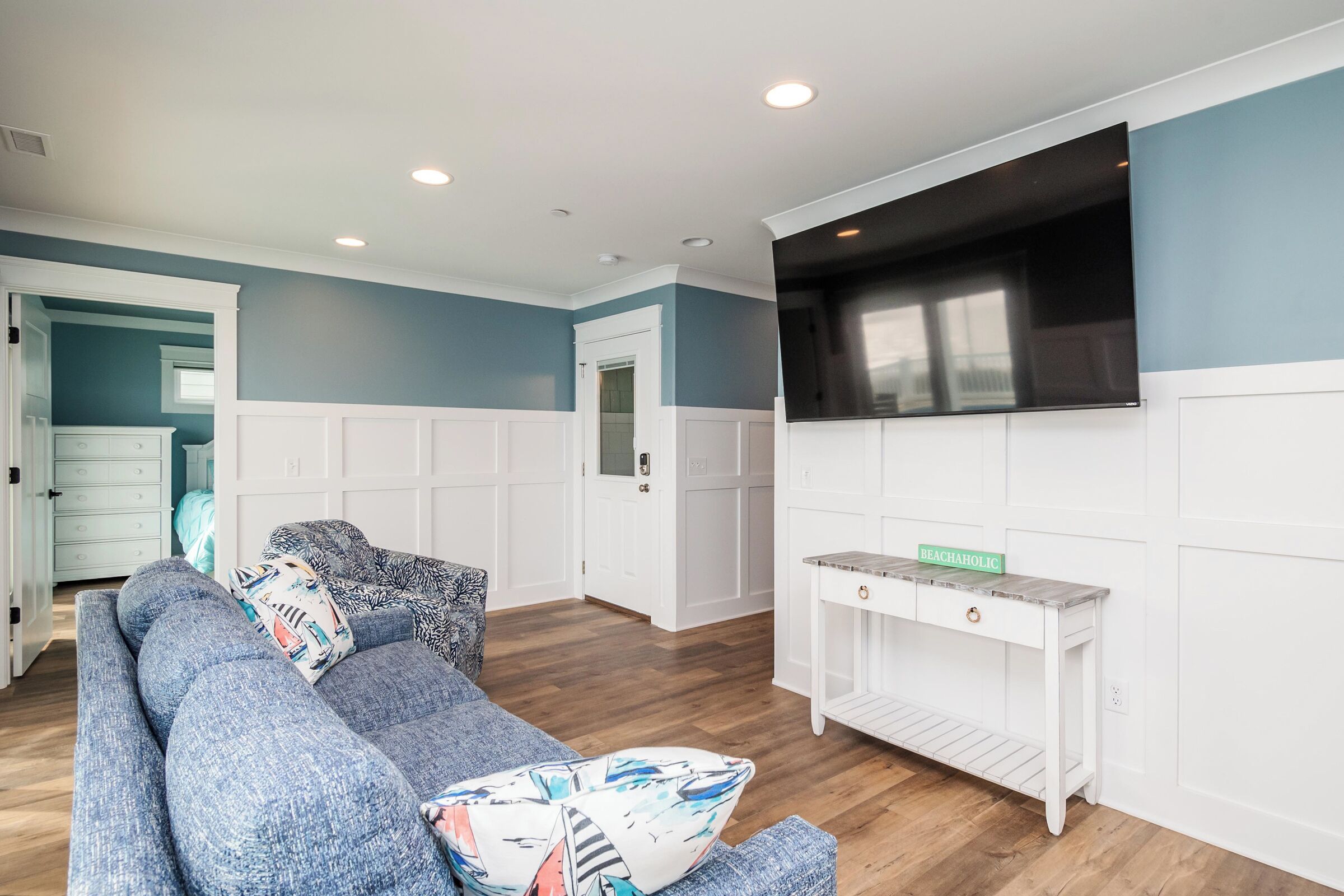 A living room with a blue sofa, a white console table, and a flat-screen TV mounted on the wall.