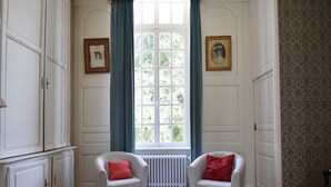 Um quarto com duas poltronas brancas, uma janela com cortinas azuis e um radiador.