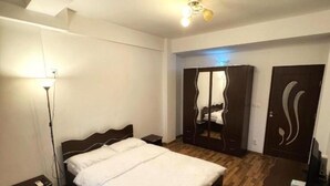 A bedroom with a wooden floor, a bed, a nightstand, a wardrobe, and a desk with a chair.
