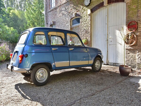 A vintage blue car parked in front of a rustic brick building with a white door and a clock on the wall. - Cottage near the Mill Pond with a beautiful garden (Le Ponchel)