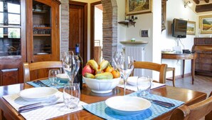 Zona pranzo con tavolo in legno apparecchiato per quattro persone, una ciotola di frutta e bicchieri da vino.