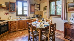 Una cucina con mobili in legno, un tavolo da pranzo con sedie, un fornello e una finestra con tende.