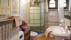 A bathroom with a glass shower enclosure, a white sink, and a wicker basket with a towel. - La Villetta by Interhome (Riparbella)