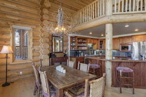 A log cabin interior with a dining area, kitchen, and a wooden staircase.