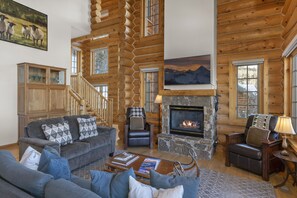 A log cabin interior with a fireplace, leather chairs, a sofa, and a bookshelf.