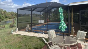 A covered outdoor area with a pool, surrounded by a glass enclosure, and furnished with chairs and a table.