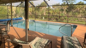 A covered outdoor pool area with lounge chairs and a view of the surrounding greenery.