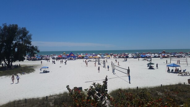 A beach with a volleyball net, tents, and people.