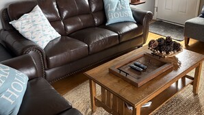 Ein Wohnzimmer mit einem braunen Ledersofa, zwei passenden Zierkissen, einem Couchtisch mit Tablett und einem gerahmten Bild über dem Sofa.