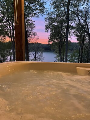 Een bubbelbad met uitzicht op een meer en bomen bij zonsondergang.