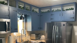 Eine Küche mit blauen Schränken, Edelstahlgeräten, einer Arbeitsplatte aus Granit und einem Fenster mit Blick auf Grünflächen.