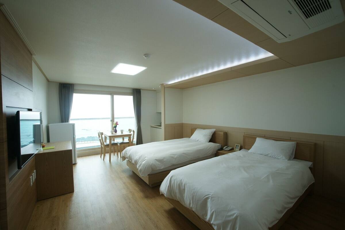 Quarto de hotel com duas camas, uma escrivaninha, uma cadeira, uma televisão e uma janela com vista.
