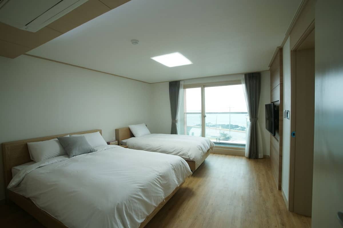Quarto de hotel com duas camas, uma televisão e uma janela grande com vista para o mar.