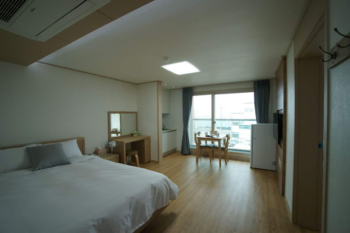 Quarto de hotel com cama, escrivaninha, cadeira, mesa pequena, televisão e janela com cortinas.