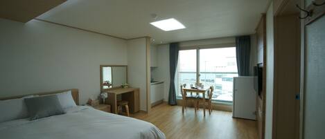 Une chambre d’hôtel comprenant un lit, un bureau, une chaise, une petite table, un téléviseur et une fenêtre avec des rideaux.