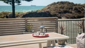 Una terrazza in legno con un tavolo apparecchiato per la colazione, con vista su un corpo d'acqua e un paesaggio collinare.