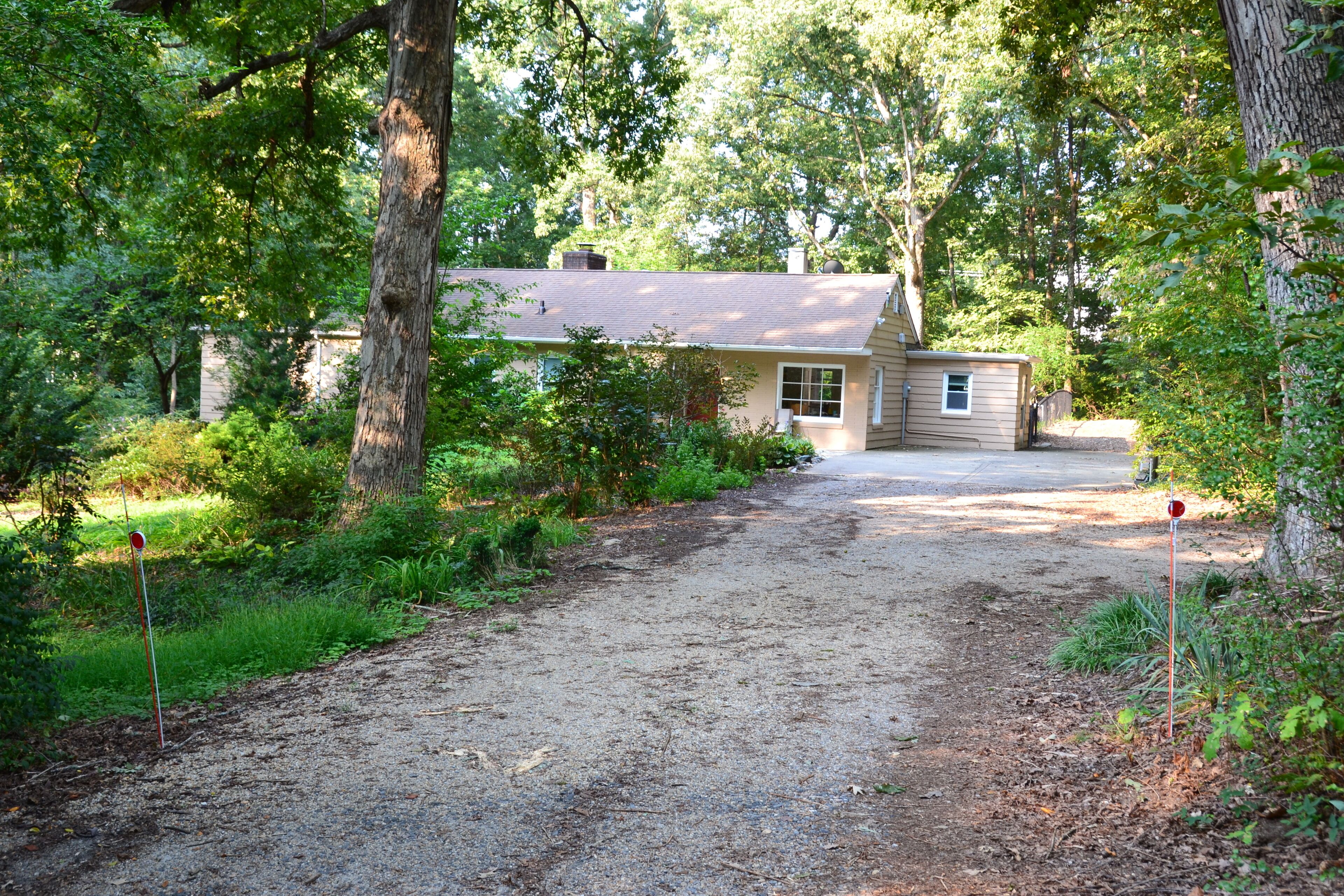 Une maison avec une allée en gravier, entourée d’arbres et de verdure.