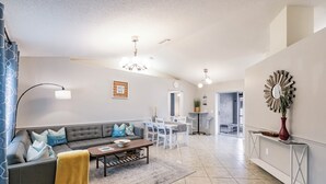 A modern living room with a grey sofa, a coffee table, and a dining area with white furniture. - 8 min to Beach ★ 5TV★Air Hockey★ BBQ★ Bikes★Baby Gear ★Table Tennis ★Beach Gear (Venice)