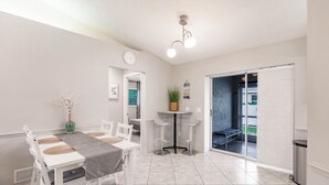 A modern dining area with a white table and chairs, a small round table with stools, a potted plant, and a wall clock. - 8 min to Beach ★ 5TV★Air Hockey★ BBQ★ Bikes★Baby Gear ★Table Tennis ★Beach Gear (Venice)
