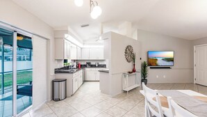 A modern kitchen with white cabinets, a dining area with a marble table, and a large TV on the wall. - 8 min to Beach ★ 5TV★Air Hockey★ BBQ★ Bikes★Baby Gear ★Table Tennis ★Beach Gear (Venice)