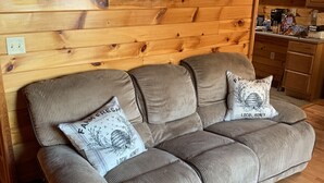 A wooden cabin interior with a sofa, pillows, a framed picture, and a kitchen area. - Private House with Great View (Afton)