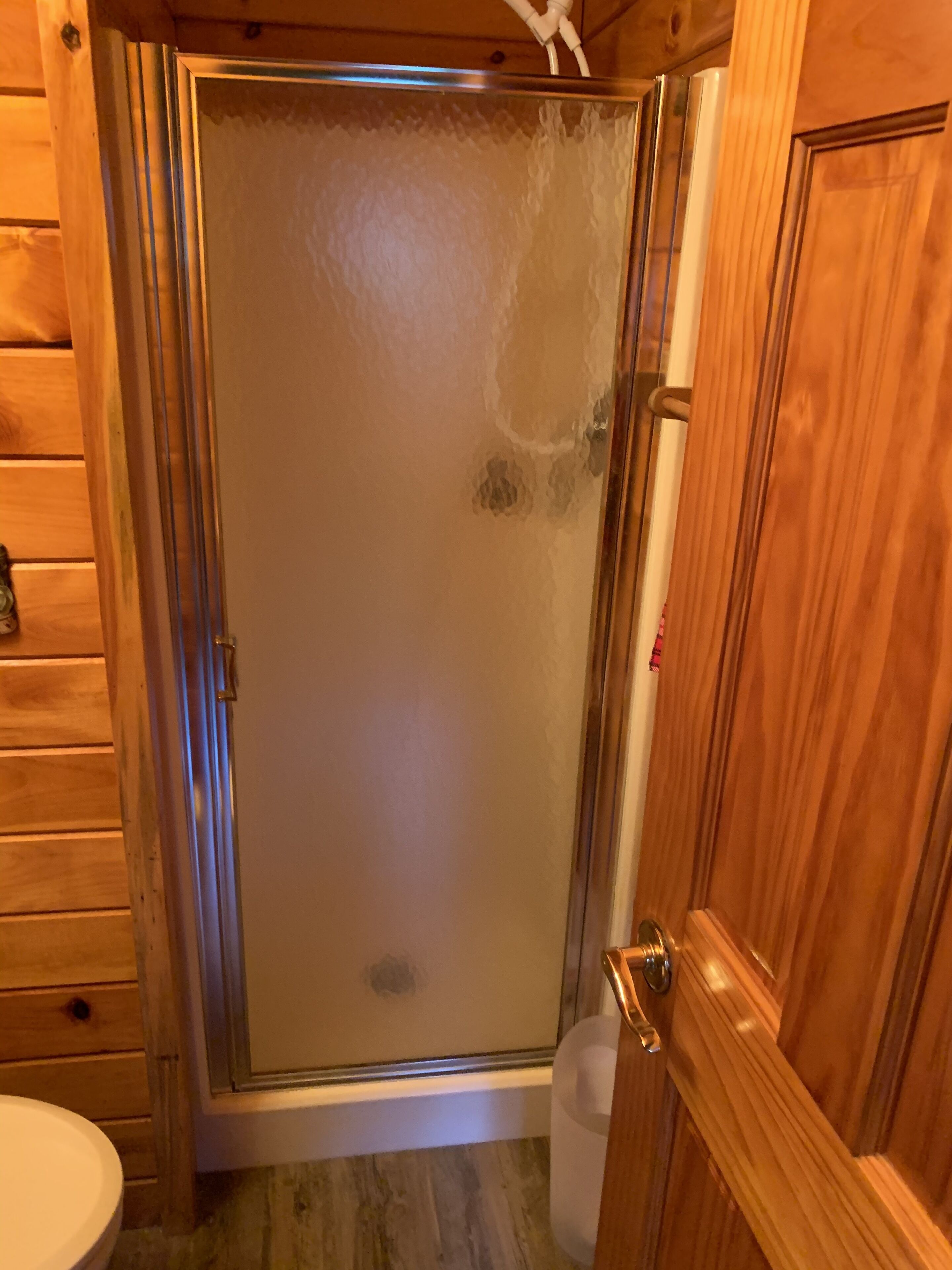 Une salle de bain en bois avec une douche en verre, des toilettes et une porte en bois.