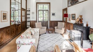 Un salon spacieux avec un canapé à motifs floraux, deux fauteuils, un meuble en bois et une radio ancienne.