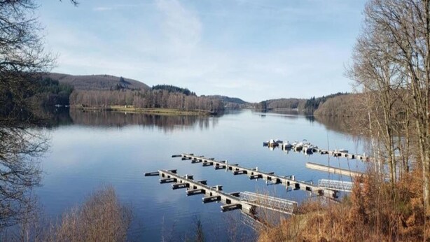 A calm lake with docks and boats, surrounded by hills and trees. - Holiday Home in Limousin near Forest (La Veytisou)