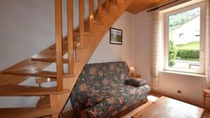 A wooden staircase, a floral sofa, a wooden table, and a window with a view of greenery.