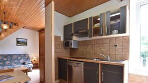 A compact kitchen with dark cabinets, a microwave, and a dishwasher. There's a wooden dining table and a sofa in the adjacent living area.